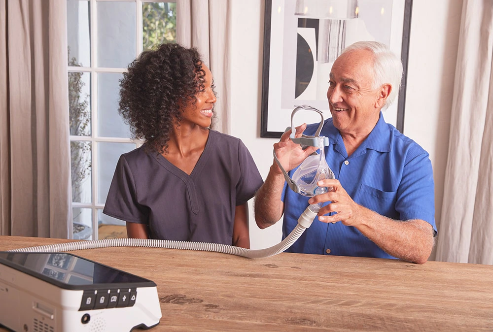 A warm, inviting healthcare facility with the Varolyn Healthcare logo prominently displayed. In the foreground, a smiling patient conversing with a compassionate nurse, their body language exuding care and trust. The middle ground showcases a cozy, well-equipped examination room, with state-of-the-art medical equipment and soothing decor. The background depicts a serene, natural landscape visible through large windows, creating a calming atmosphere. The lighting is soft and diffused, lending an air of comfort and tranquility. The entire scene conveys Varolyn Healthcare's commitment to patient-centered care, where the well-being and comfort of individuals are the top priorities. ventilator support at home